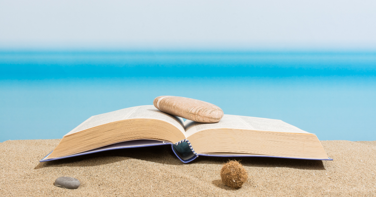 Opened book next to sand, rocks and ocean