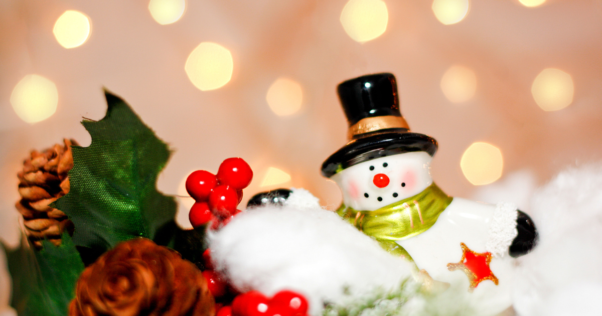 Ceramic snowman in front of holiday greenery.