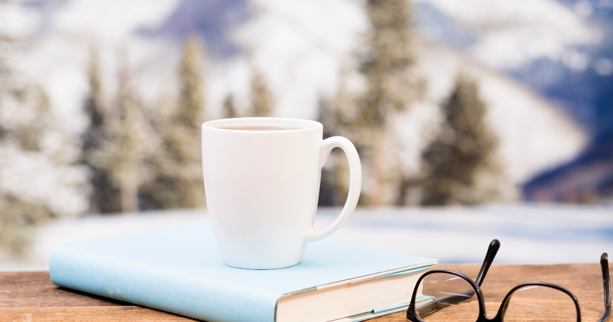 White coffee cup on book with mountain and snow as backdrop